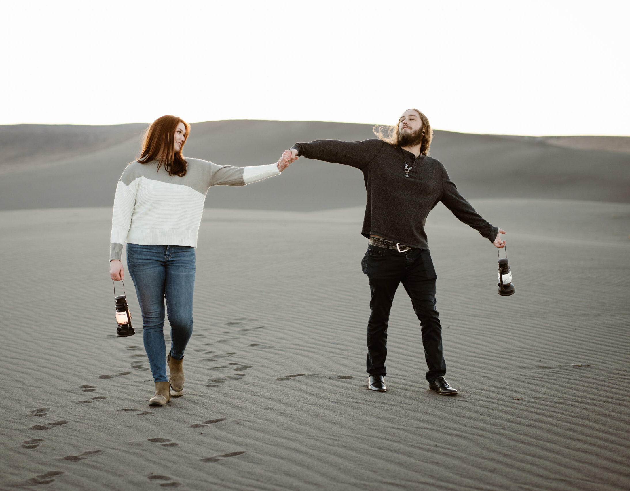 Couple poses for their engagement photos on sand dunes with lanterns.